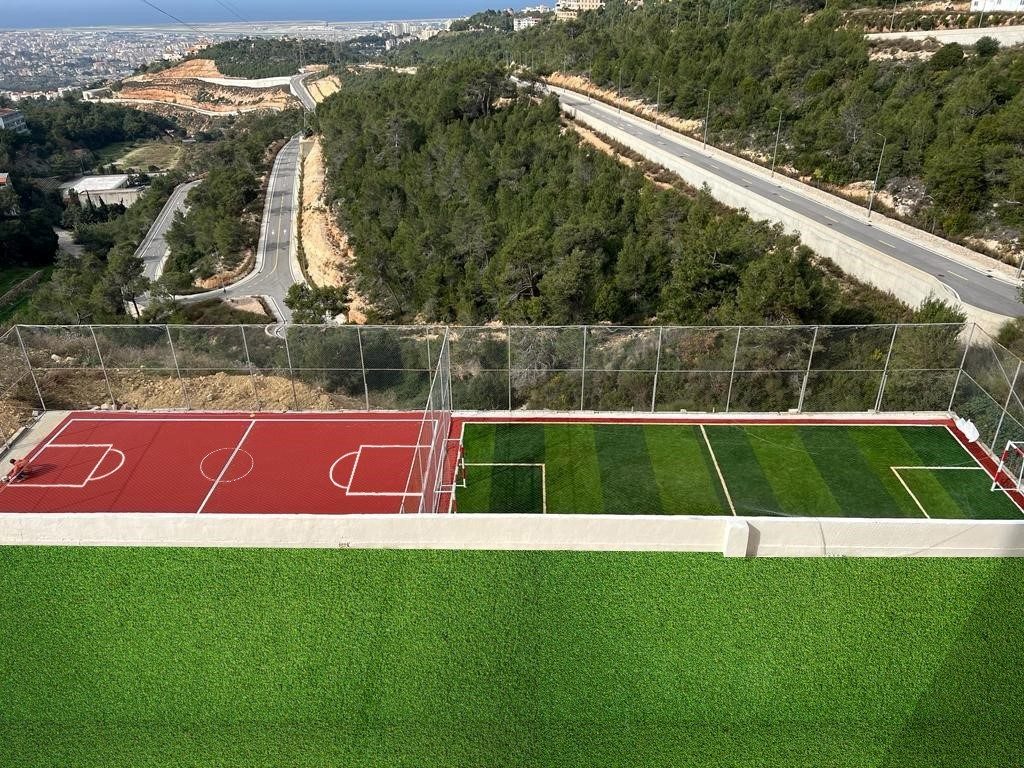 The sports courts perched above the wooded valley with the coast beyond